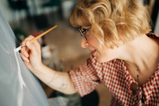Smiling female artist painting fine details on canvas close-up