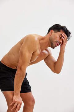 Man holds head with hand while standing against a plain wall