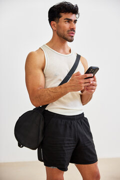 Man in workout clothes checks phone in indoor space