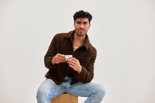 Man sitting on a stool holding a cup in a light room