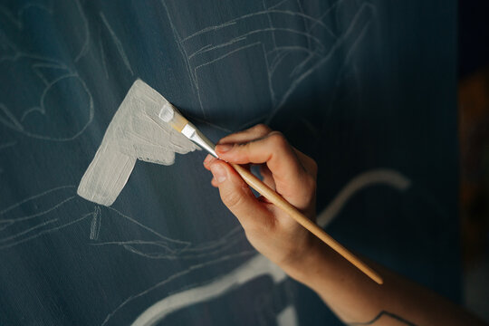 Close-up of artist painting white base layer on textured canvas