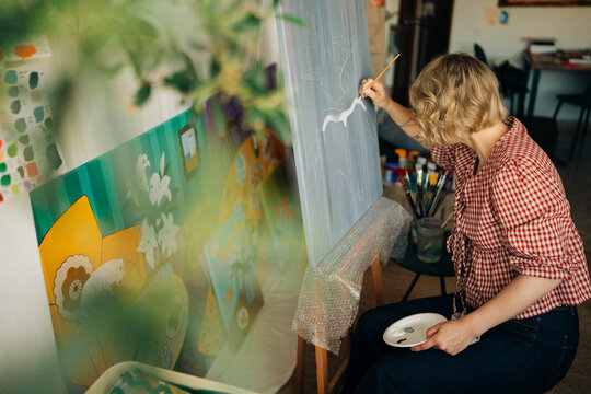 Creative woman painting on canvas with blurred foreground leaves
