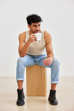 Man sitting on wooden block and holding cup in modern room