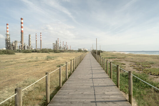 Long wooden path leading toward oil refinery and coastal horizon