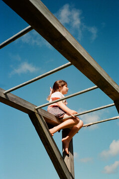 Young girl sitting on top of monkey bars in Australian Front Yard.
