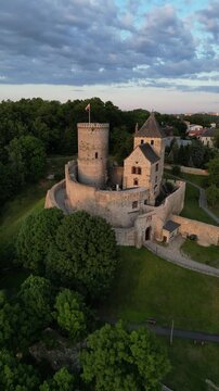 Vertical aerial drone tracking shot pushing in on the medieval Bedzin Castle in Poland, revealing detailed stone fortress architecture, courtyard and waving national flag.