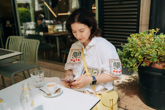 Young Woman Using Smartphone at Outdoor Cafe
