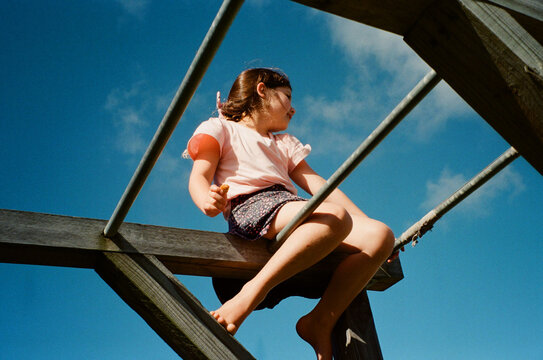 Young girl sitting on top of monkey bars in Australian Front Yard.