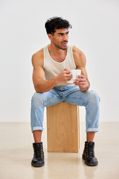Man drinks coffee while sitting on a wooden box in a simple room