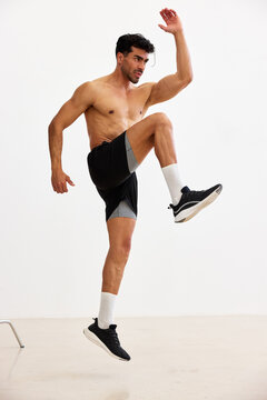 Man exercises indoors with high knees on a light background