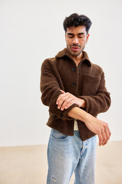 Man adjusting his brown jacket in a simple room setting