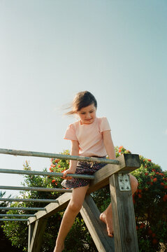 Young girl sitting on top of monkey bars in Australian Front Yard.