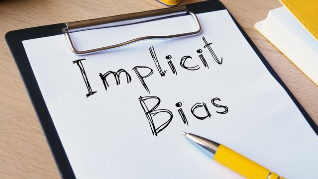 Implicit bias written on a white paper on a black clipboard with a pen on a desk implicit prejudice clipboard discrimination