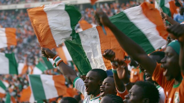 Closeup view of Ivory Coast fans energetically waving flags celebrating and chanting as the continental soccer match unfolds in a fullcapacity stadium.