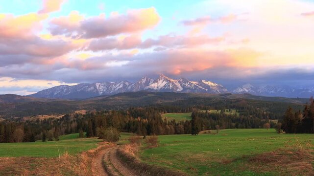 Beautiful sunset over snow covered mountain peaks and green meadows