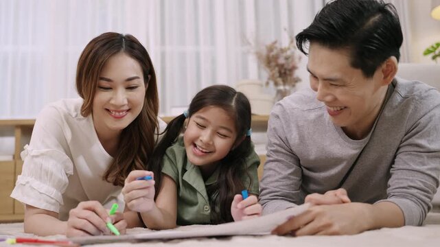 Happy Asian Family Day Concept. Smiling father mother and daughter relaxing and painting on paper together in living room at home. Activity leisure of dad mom and child girl cheerful and fun to draw.