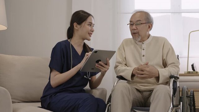 Professional young Asian woman nurse caregiver using a digital tablet to talk and provide advice about healthcare to a senior man patient while sitting in a wheelchair in a special room at hospital. 