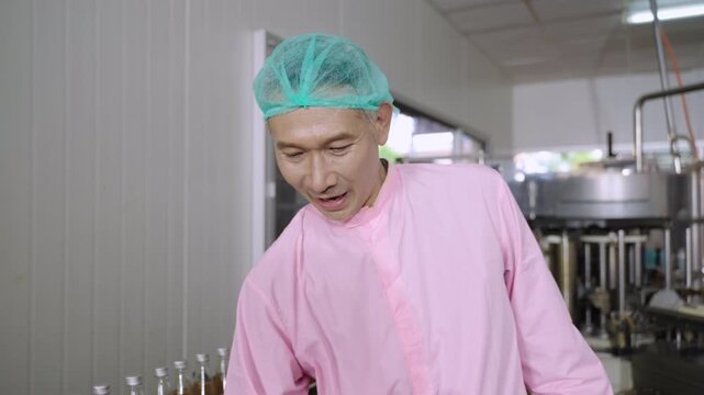 Professional Asian inspector in uniform of food and drink factory holding a juice beverage bottle promoting and advertising healthy nutritional benefits in production line at a manufacturing industry.
