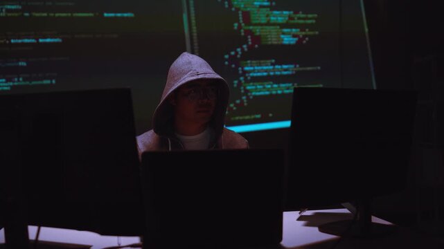 Hacker Working with Multiple Computer Screens Displaying Code in a Dark Setting