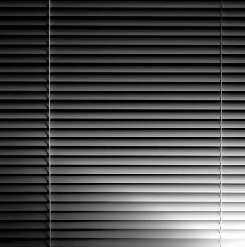 Venetian window blinds at night with glow from lamp light in black and white monochrome