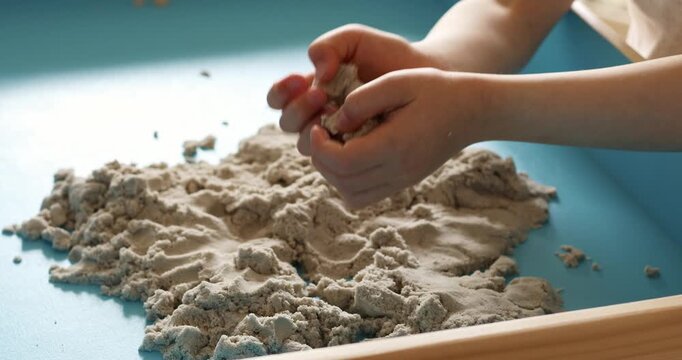 Children activity with kinetic sand for motor and sensory development. Toddler play therapy on wooden sandbox. at home