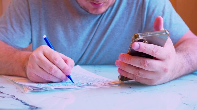 Cinematic close up shot of using a cellphone screen to cross-reference data on paperwork with a felt pen.Visualizes distance learning, accounting, verification and business planning.