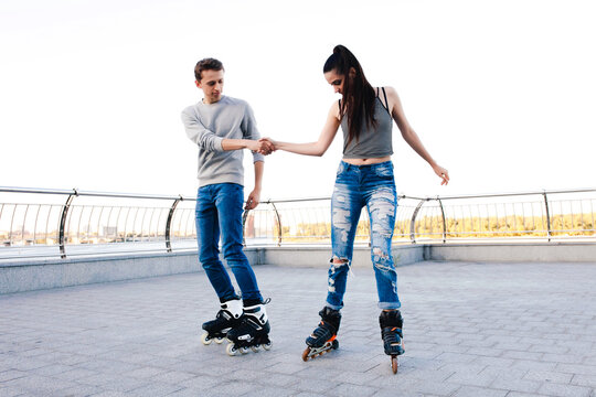 Young couple inline rollerblading on a pier, man helping woman
