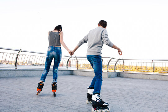 Young couple holding hands rollerskating outdoors enjoying leisure