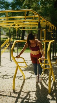 A fit woman performs push-ups on parallel bars at an outdoor gym. She demonstrates strength and an active lifestyle with her calisthenics.