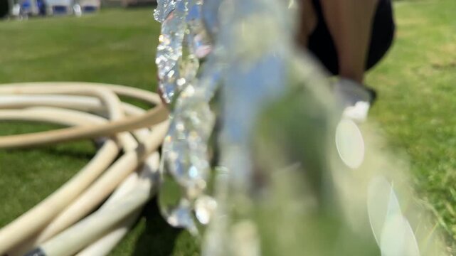 Gardener turns on water faucet, hose sprays lawn, sunny irrigation, fresh green grass, outdoor chore.