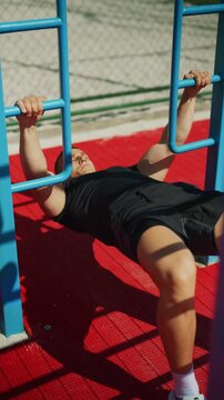 A man performs inverted rows on an outdoor fitness rig. He is building upper body strength during his workout.