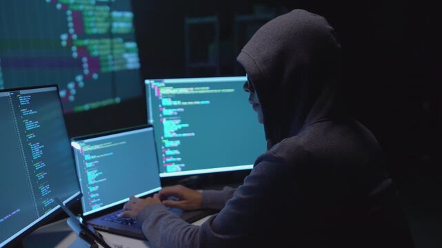 Hacker Typing Code on Multiple Screens in a Cybersecurity Environment