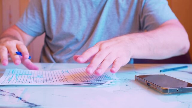Low angle close-up of hands filling a document and verifying data on a smartphone. Shallow DoF, natural light. Metaphor for mobile banking, two-factor authentication, online tax filing and remote work