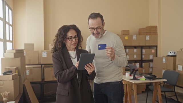 Man and woman pointing at tablet while man holds creditcard inside a storage building; efficient collaboration trust.