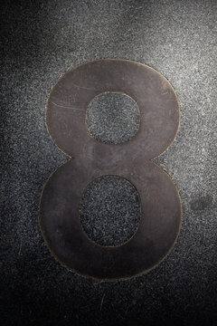 Large number eight in a dark setting on a textured surface showing shadows and highlights