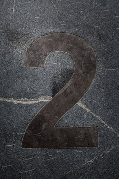 Round dark number two on a gray surface with cracks and lines during daylight