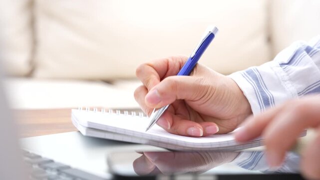 Business professional preparing notes while reviewing information from smartphone and laptop. Workflow planning, documentation process, task management, digital productivity and paperless business con