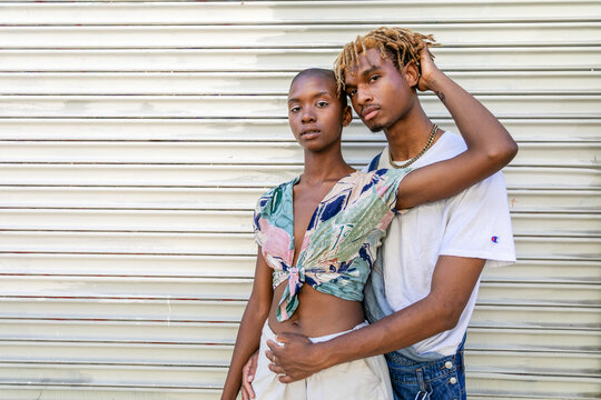 Two people embracing in front of a metal shutter, casual attire.