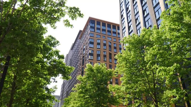 Modern residential building shot through green trees in downtown. Urban nature and architecture. nature and development. Business District with Corporate Futuristic Cityscape. 4 k video