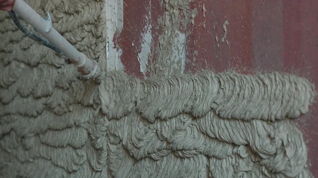 Spraying plaster mortar onto wall with plastering machine