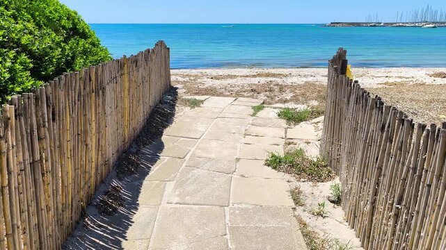 Slow motion reveal from ground level on a path to the sea with camera rising to reveal a coastal beach and shoreline scenery.