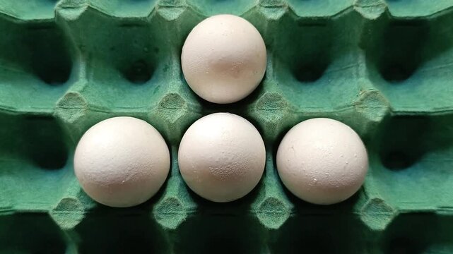 Four fresh white chicken eggs in triangle shape inside a green pulp carton tray