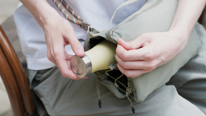 Naklejka premium Hands putting a reusable thermos water bottle into a special compartment in a stylish streetwear bag, convenient and practical accessories