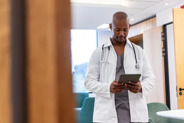 African American adult male doctor standing in clinic wearing lab coat and stethoscope using tablet © wavebreak3