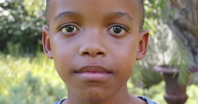 African male child responding to camera, relaxing face, smiling in garden by tree trunk and urn