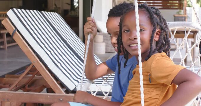 African American kids on patio swing holding ropes, camera panning, right child leaning to camera