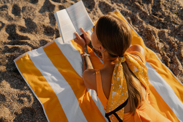 beautiful blond woman lying on beach reading book on summer season vacation wearing yellow swimsuit © mary_markevich