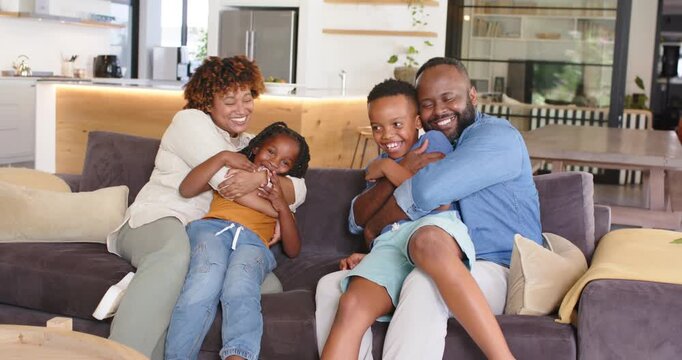 African American family on dark sofa in open living room, parents pulling kids closer, showing love