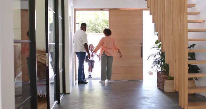African American family greeting youths entering front door, adjusting backpacks in foyer
