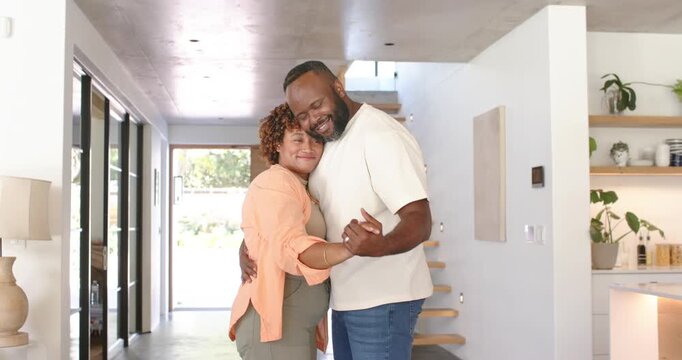 African American couple hugging, man leaning head, swaying in entry by floating stairs, sharing joy